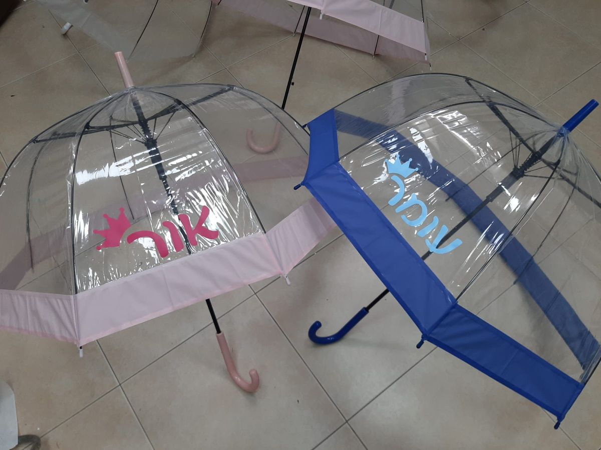 שתי מטריות שקופות עם שמות בצבעים שונים ועיטור כתר מוצבות על רצפת קרמיקה